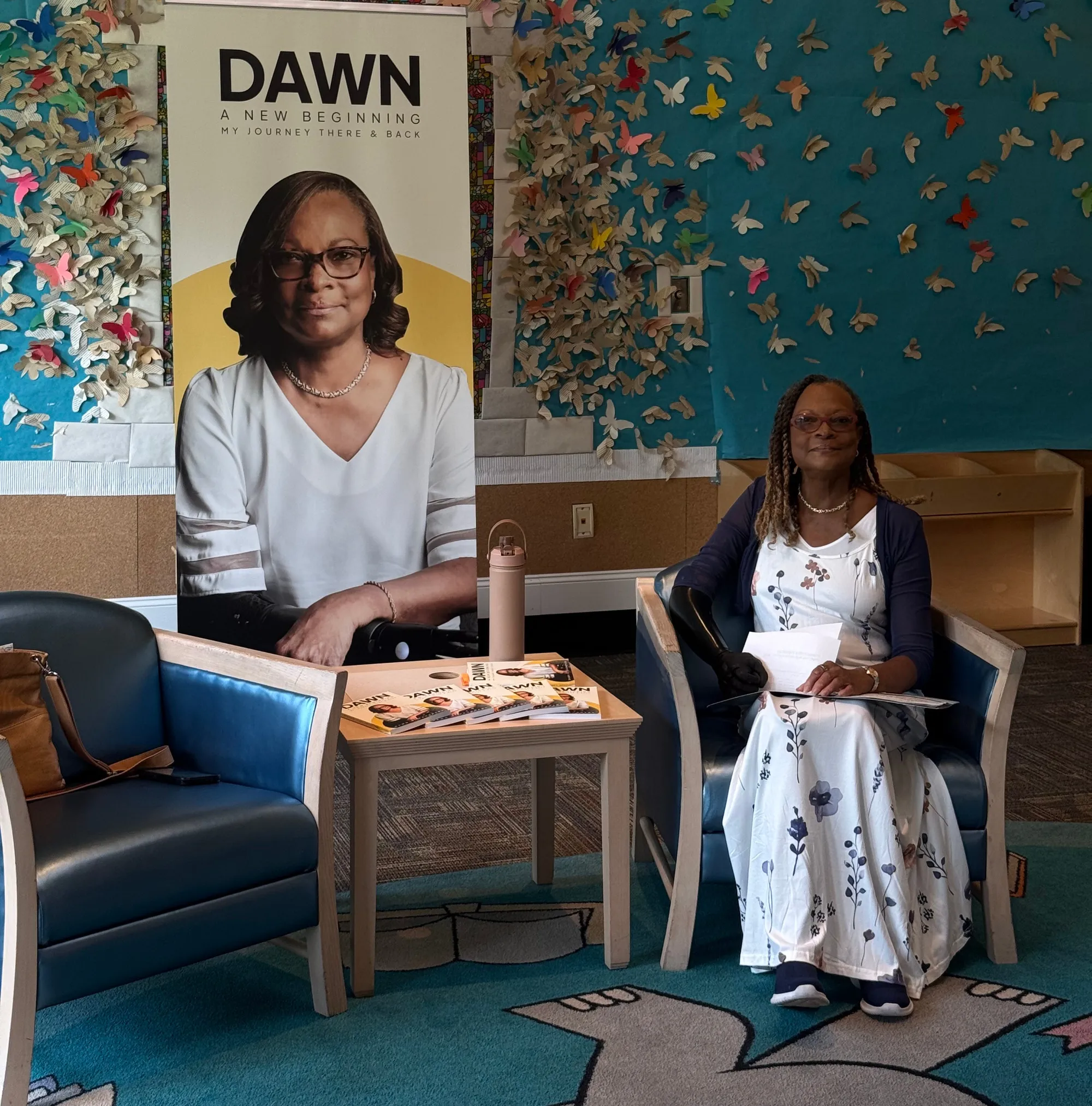 Dawn at an author event beside her book banner